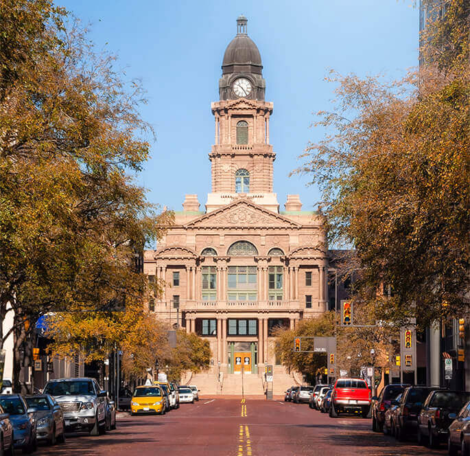 Historic courthouse building framed by autumn trees and parked cars.